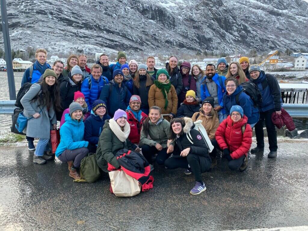 A group of 35 people gather together in front of a mountain