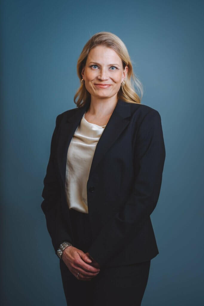 Image shows blonde woman in a black suit, smiling.