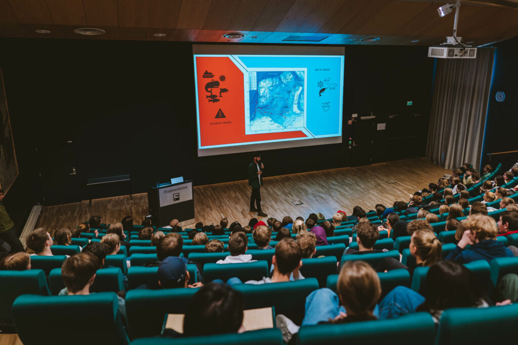 Bilde viser en forsker fra Norsk Polarinstitutt som presenterer arbeidet sitt foran elever.