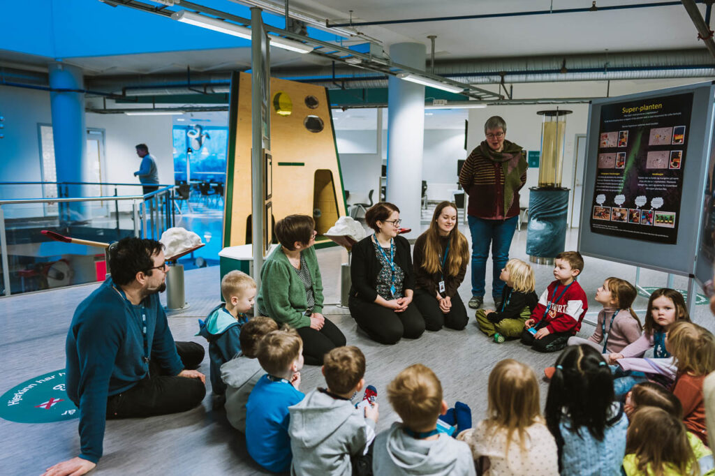 Bilde av ca. 15 barn som sitter i ring og forteller om plakaten sin på Science for Kids. 