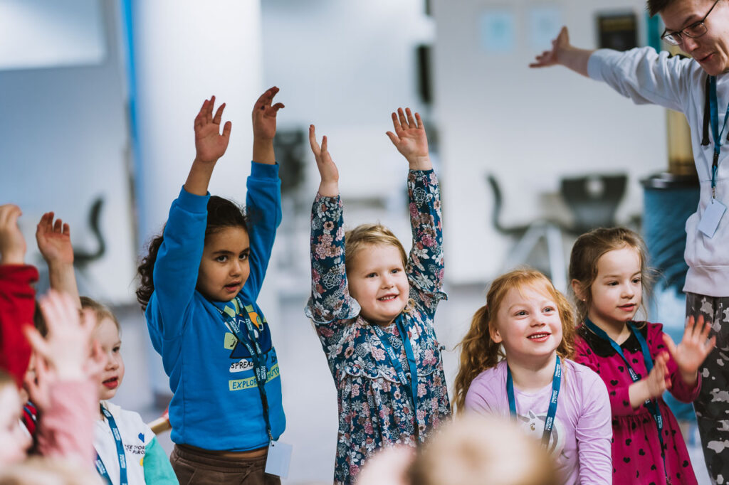 Bildet viser barn som rekker opp hendene i lufta for å feire at de er ferdige med å fortelle om plakatene sine.