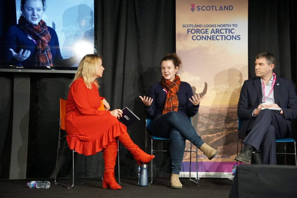 Image shows stage and three people in a panel discussion.