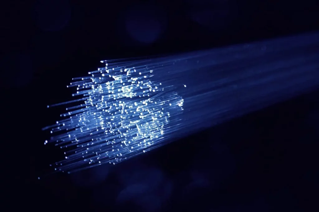 Image shows fibre cabels lit by blue light in front of a dark background