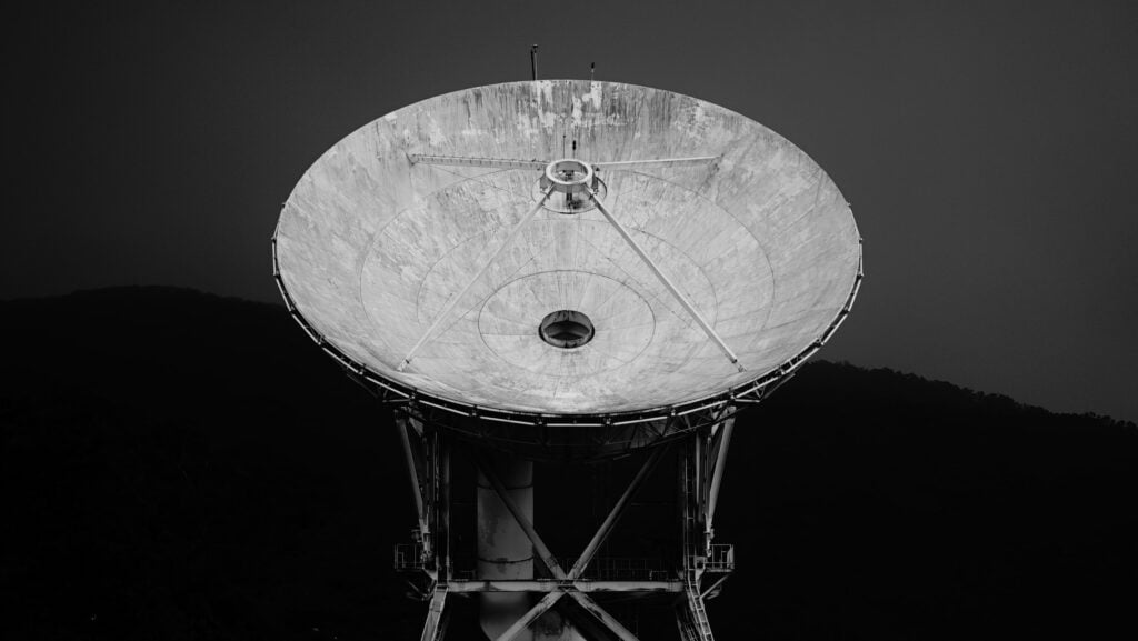 Photo shows a Satellite antenna pointing upwards. The surface is light and the image has a dark background. 