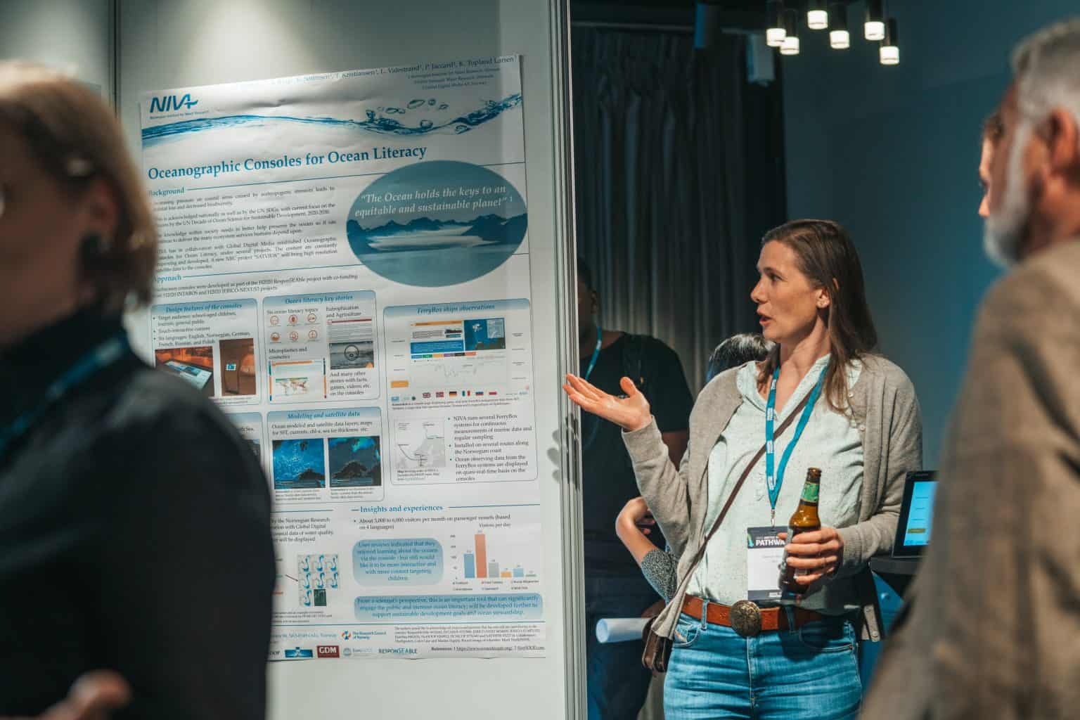 A female scientist stands in front of her poster talking to two people about her work.