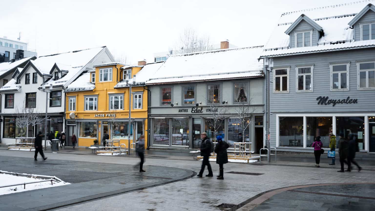 Wooden colourful shops on tromsø high street during a cloudy wet day. People walking past.