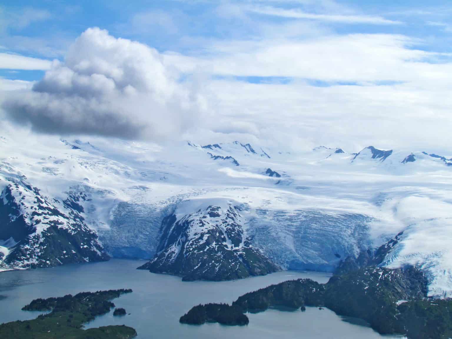 Two glaciers meet a fjord. Cloudy skies with sunshine.