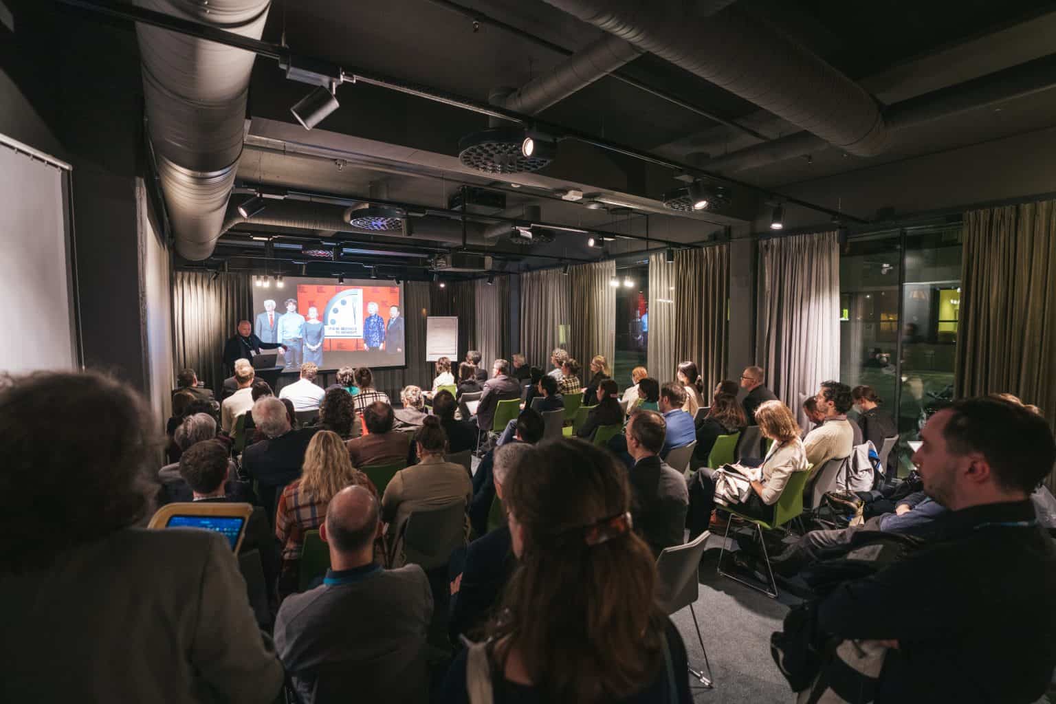 A photo from the back of a packed room of scientists and policy makers listening to someone making a presentation.