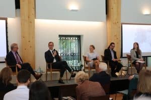 A panel with 4 speakers and a moderator in the middle are on a stage in front of an audience. The second to the left is Morten from Freyr Battery who is talking into a microphone.