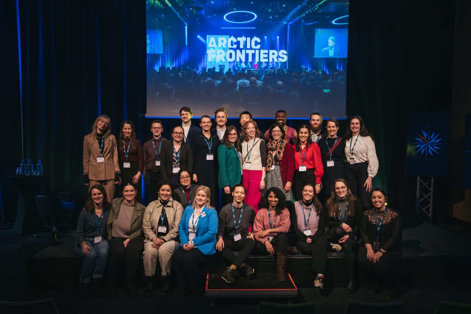 A group of 30 Emerging Leaders standing and sitting on a stage at the Arctic Frontiers 2023 conference.