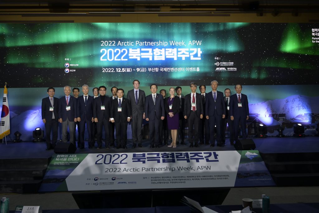 Image shows large group of people dressed in formal attire. They are standing in front of a sign that reads "2022 Arctic Partnership Week".