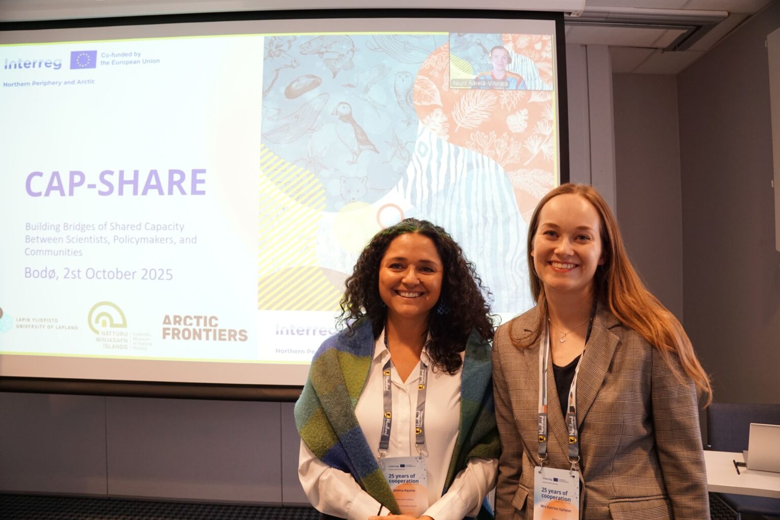 Arctic Frontiers - Two women smiling in front of a presentation slide for the Arctic Frontiers - CAP-SHARE event, scheduled for October 2025 in Bodø.