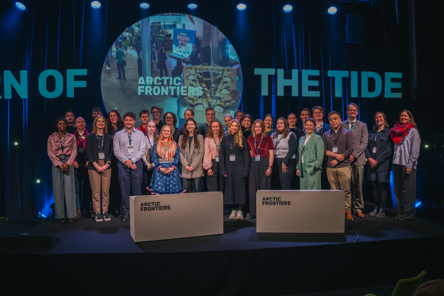 Arctic Frontiers - A group of people, including several étudiants, posing on stage at an Arctic Frontiers event, with blue lighting and two white podia.