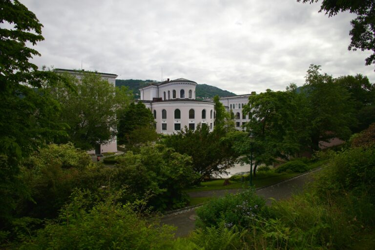 A photo of a white museum building surrounded by a green garden.