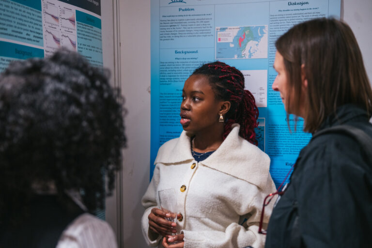 Arctic Frontiers - Three young women stand and talk in front of blue scientific posters at an Arctic Frontiers event or presentation.