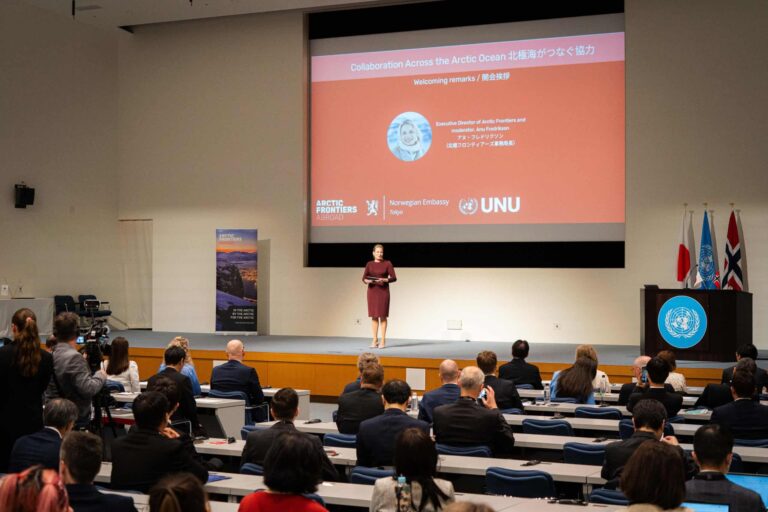 Arctic Frontiers - A woman speaks on stage at a conference in Tokyo, with an audience seated and a presentation screen behind her.