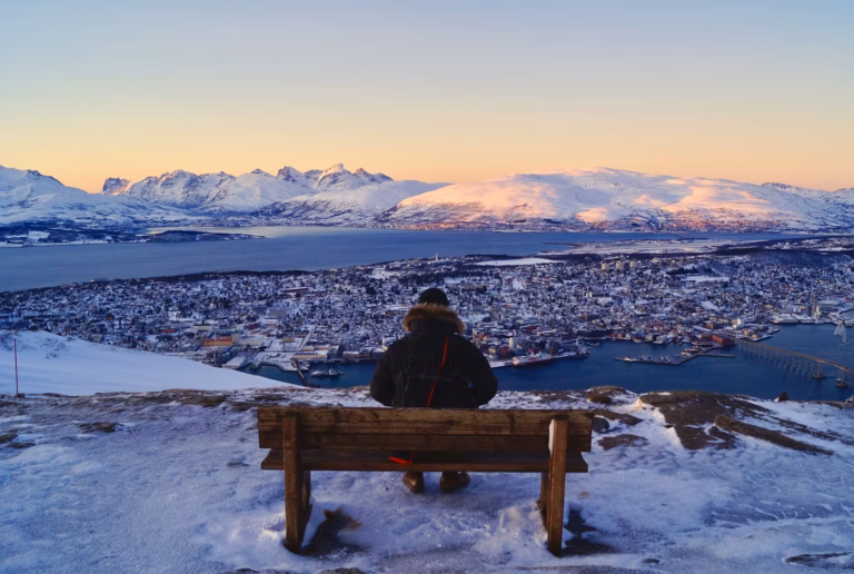 A person sitting at a bench with a view over Tromsø in winter.