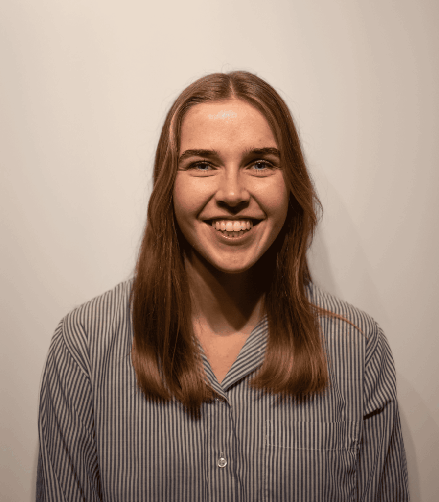 Arctic Frontiers - Elisabeth Torvik, a woman with long brown hair smiling, is wearing a striped button-up shirt and standing against a plain background.