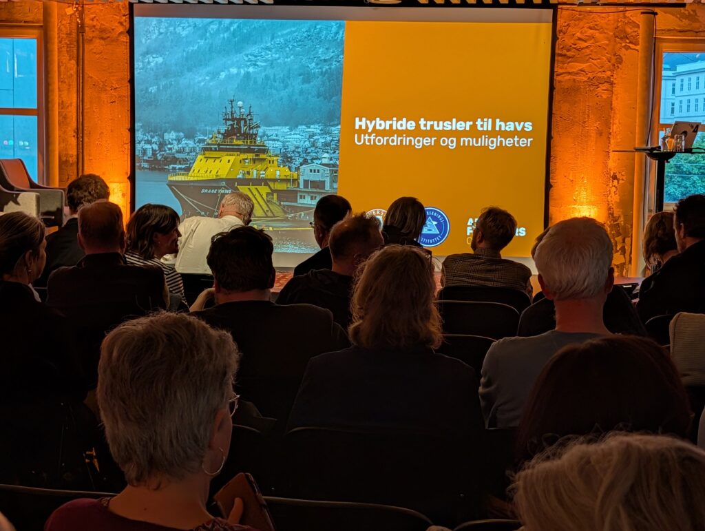Arctic Frontiers - Audience at Arctic Frontiers viewing a presentation on hybrid threats at sea with Norwegian text and a ship image.