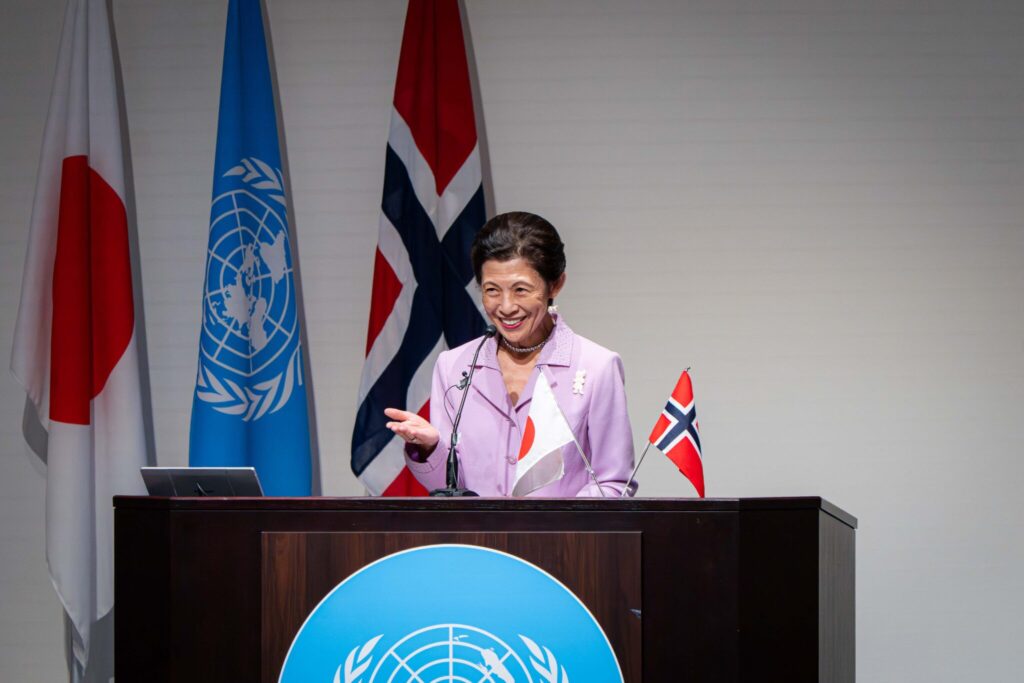 Arctic Frontiers - A woman speaks at a lectern with Japan, UN, and Norway flags in the background, addressing an audience about Arctic Frontiers during a conference in Tokyo.