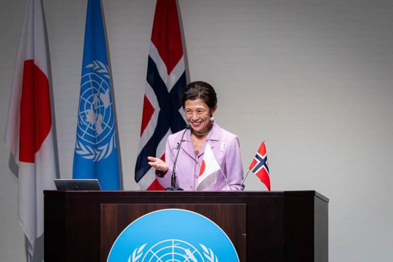 Arctic Frontiers - A woman speaks at a lectern with Japan, UN, and Norway flags in the background, addressing an audience about Arctic Frontiers during a conference in Tokyo.