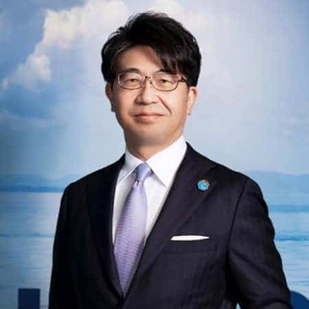 Arctic Frontiers - A man in a suit and tie standing in front of a blue sky and water background, smiling slightly.