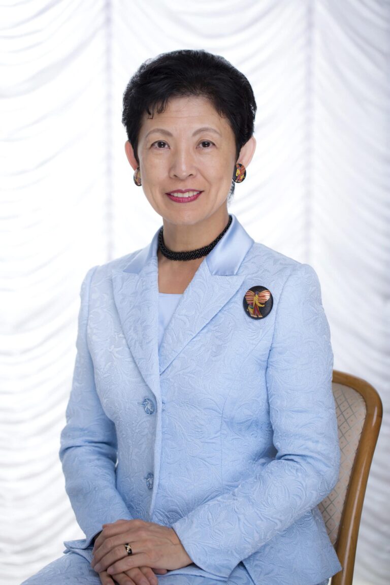 Arctic Frontiers - A woman in a light blue suit sits on a chair, smiling, in front of a white, patterned backdrop.