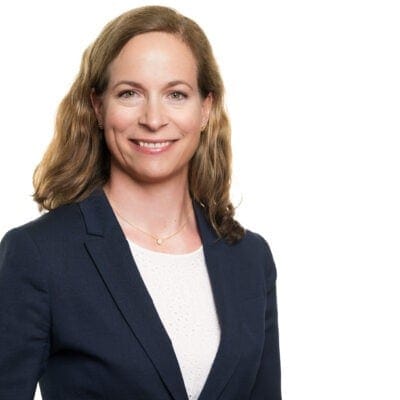 Arctic Frontiers - Smiling woman with wavy brown hair in a navy blazer and white top, posing against a white background.