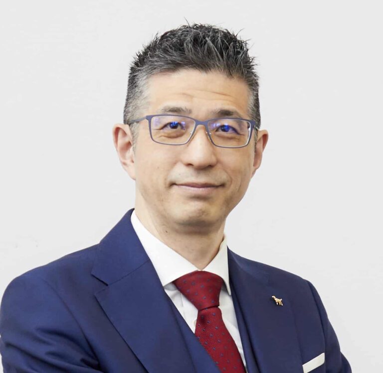 Arctic Frontiers - Man with short dark hair and glasses wearing a navy suit, white shirt, and red tie, smiling slightly.