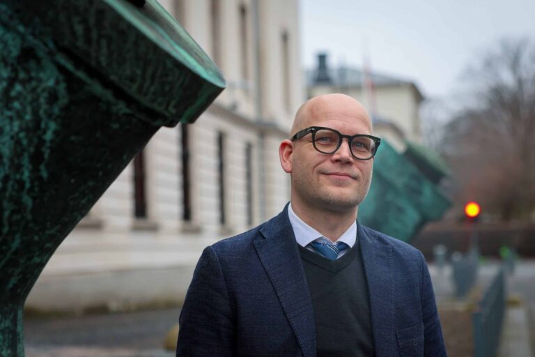 Arctic Frontiers - Bald man in glasses and a suit standing outside near a building with green sculptures.