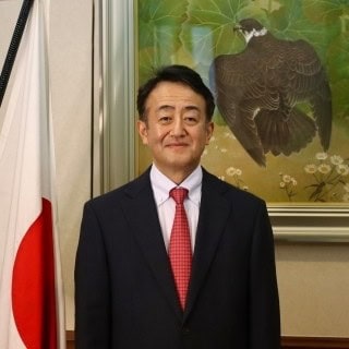 Arctic Frontiers - A man in a suit stands by a Japanese flag, with a bird painting in the background.