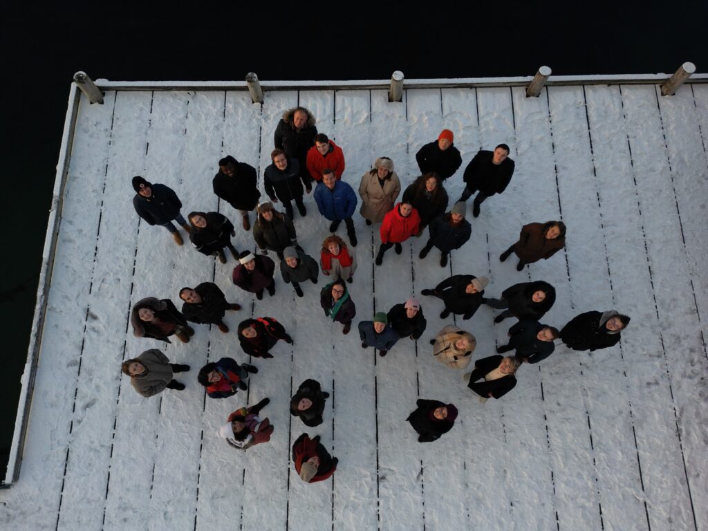 Arctic Frontiers - A group of people, including emerging leaders, stand on a snowy wooden jetty, looking up at the camera from above—capturing the spirit of collaboration often seen at Arctic Frontiers.