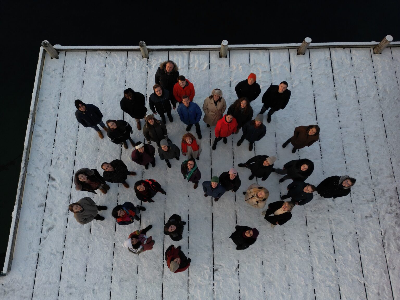 Arctic Frontiers - A group of people, including emerging leaders, stand on a snowy wooden jetty, looking up at the camera from above—capturing the spirit of collaboration often seen at Arctic Frontiers.