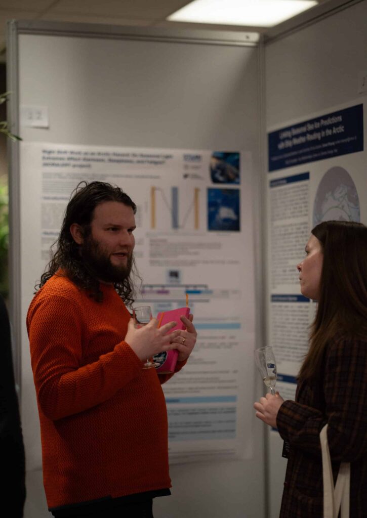 Arctic Frontiers - Two people talk in front of scientific posters at a conference, holding glasses and papers.