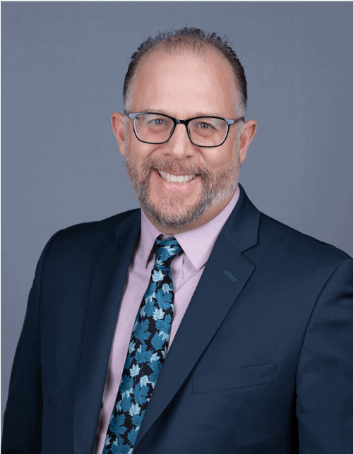 Arctic Frontiers - A portrait of a resilient man with glasses, a beard, and a suit and tie smiling.
