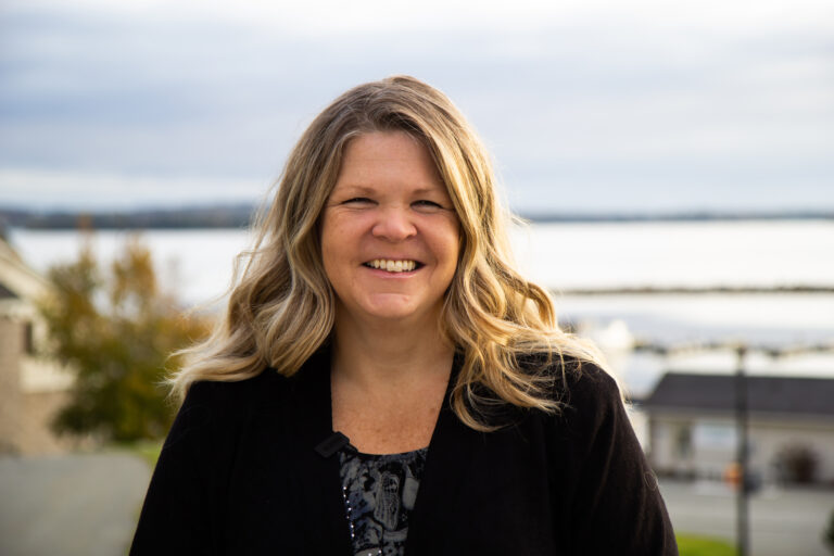 Arctic Frontiers - A smiling woman standing outdoors by an Arctic lake, embodying a sense of resilience.