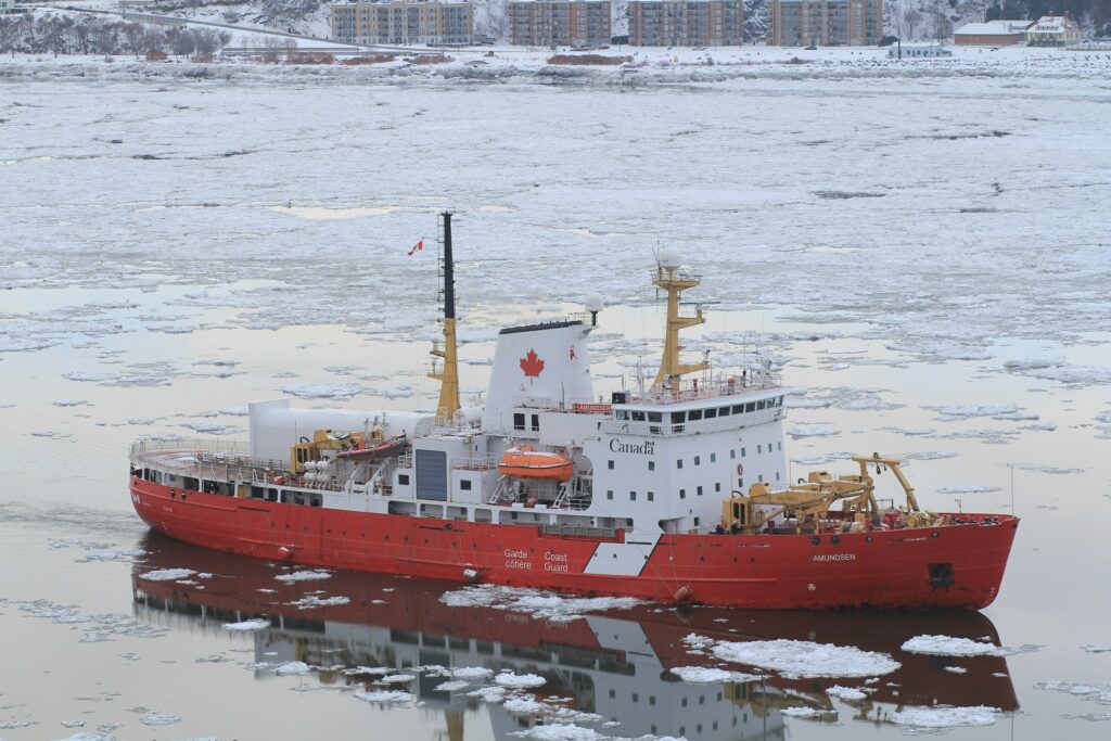 Arctic Frontiers - A red and white Canadian Coast Guard icebreaker sails through icy water.